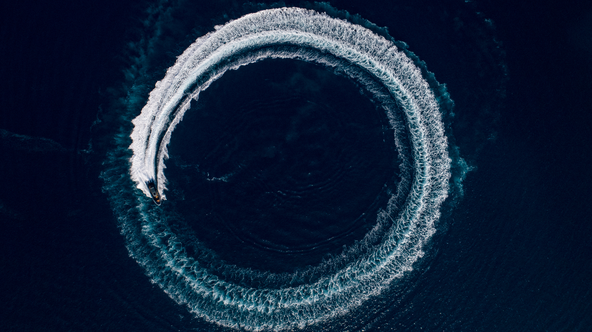 Aerial drone view of a RIB carving a perfect circle of wake on deep blue water